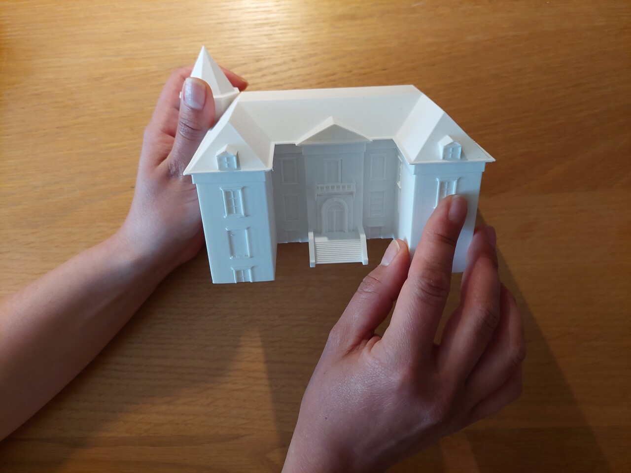 Twee handen houden een 3D print van een huis vast.